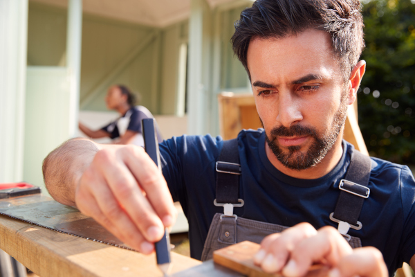 male carpenter with female apprentice measuring wood