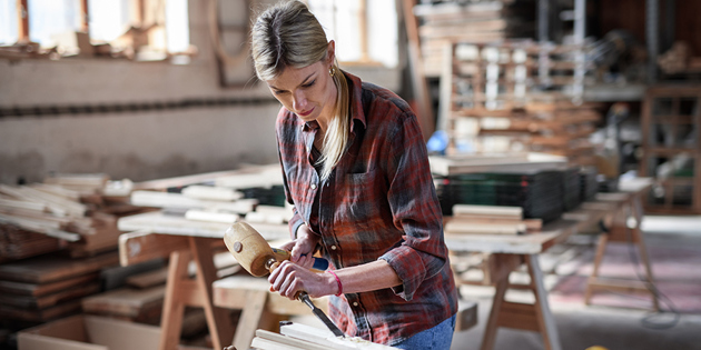 A portrait of female carpenter working on her product indoors in carpentry workshop.